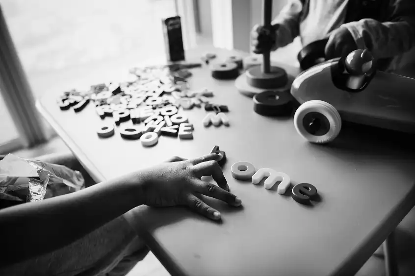Een kind legt plastic letters op een tafel om woorden te vormen, met ander educatief speelgoed op de achtergrond.